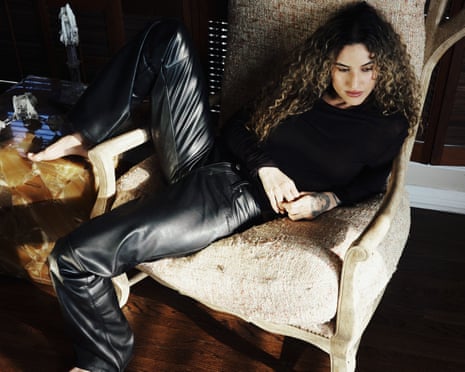 Lorely Rodriguez AKA Empress Of sitting sideways on a cream armchair, wearing leather trousers