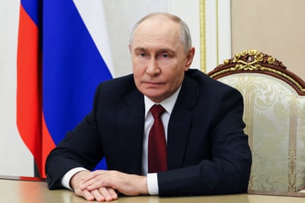 Putin sitting at a table in front of a Russia flag