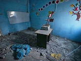 A colourful cut out of a tree and flowers on bright blue walls of a rubble-strewn classroom.