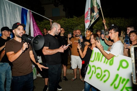 A man with a megaphone, others with placards and flags.