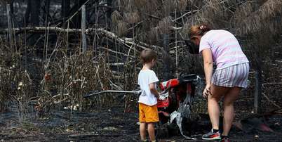 Uma m&atilde;e e seu filho inspecionam os arredores de sua casa em Le Porge, na segunda-feira, ap&oacute;s ela ter sido destru&iacute;da por um inc&ecirc;ndio florestal Foto: Reuters / BBC News Brasil